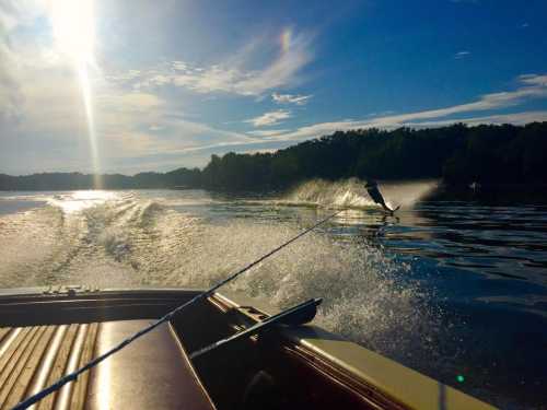 A person water skiing behind a boat on a sunny lake, with splashes and reflections on the water.