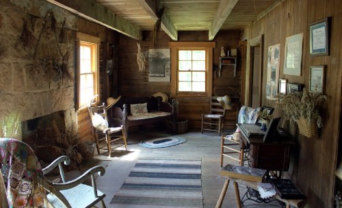 Cozy rustic interior with wooden walls, a seating area, and vintage decor, featuring a woven rug and natural light.