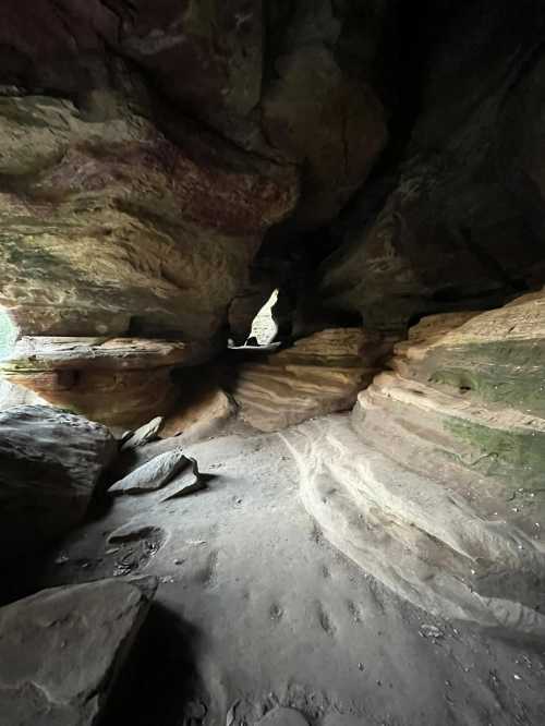 A rocky cave with colorful layered walls and a narrow opening, illuminated by soft light from outside.