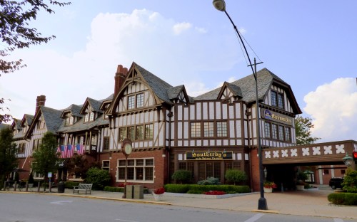 Historic building with Tudor-style architecture, featuring flags and a sign for "Southeby's." Clear blue sky in the background.