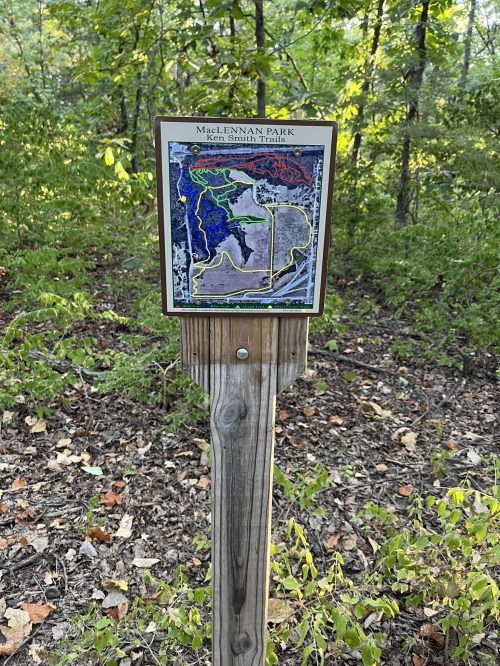 Map sign for McLennan Park, showing trails and park layout, surrounded by greenery.