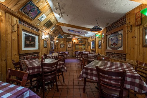 Cozy restaurant interior with wooden walls, checkered tablecloths, and vintage decor, featuring empty tables and warm lighting.