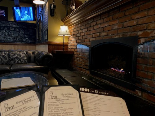 Cozy restaurant interior with a brick fireplace, menu on a table, and a TV showing a program in the background.