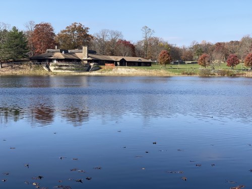 A serene lake reflects a rustic building surrounded by autumn trees and clear blue skies.