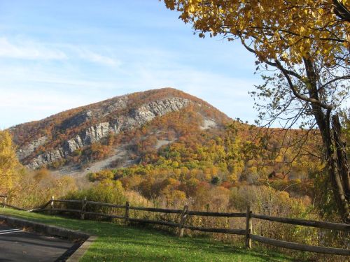 A scenic view of a mountain covered in autumn foliage, with a wooden fence in the foreground and a clear blue sky.