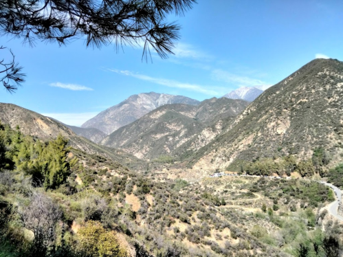 Scenic view of mountains and valleys under a clear blue sky, with greenery and a winding road in the foreground.