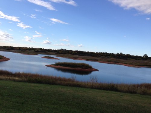A serene landscape featuring a calm lake with small islands and lush greenery under a blue sky with scattered clouds.
