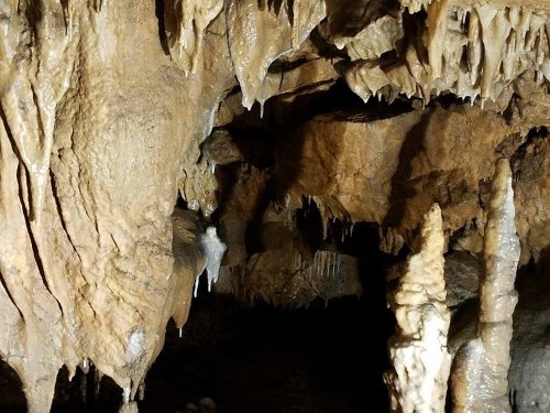 A dimly lit cave interior featuring stalactites and stalagmites with dripping water and rocky textures.