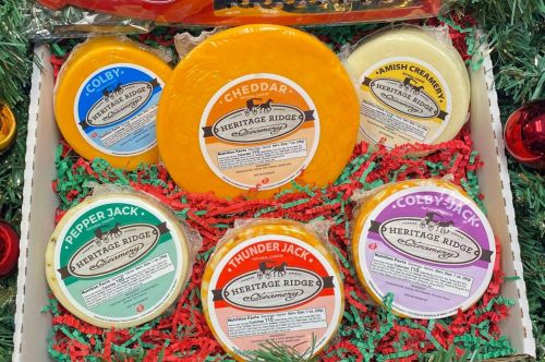 A festive cheese gift box featuring various cheese types, including Cheddar, Colby, and Pepper Jack, on colorful filler.