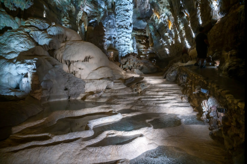 A dimly lit cave with textured rock formations and illuminated pools of water, creating a mystical atmosphere.