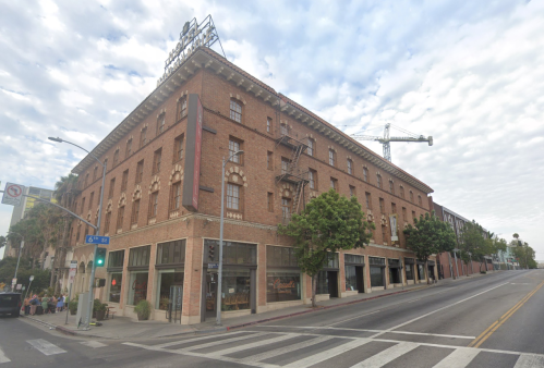 Historic brick building on a street corner, featuring large windows and a rooftop sign, with a crane in the background.