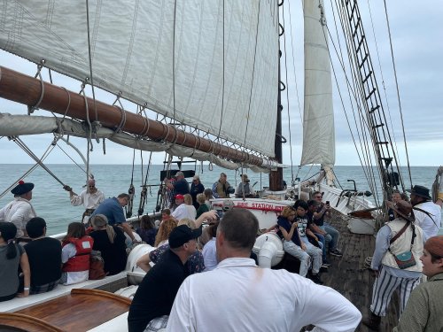 A group of people on a sailing ship, enjoying a trip on the water with sails raised and cloudy skies above.