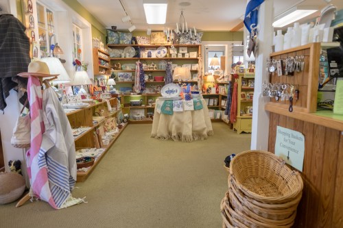 A cozy shop interior filled with colorful merchandise, shelves, and a central display table surrounded by baskets.