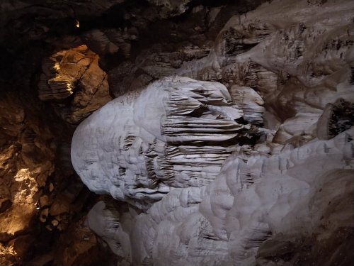A large, white stalagmite resembling a face, surrounded by textured rock formations in a dimly lit cave.
