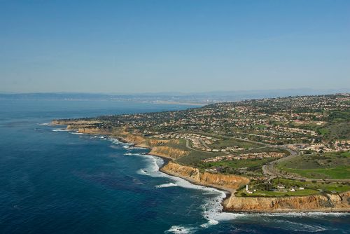 Aerial view of a coastal landscape with cliffs, ocean waves, and a residential area along the shoreline.