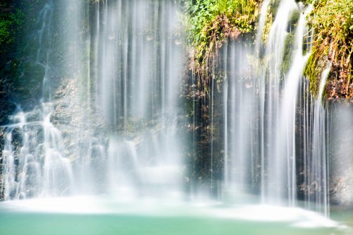 A serene waterfall cascading over rocks, creating a misty atmosphere and pooling in a tranquil green basin below.