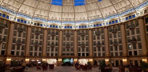 Interior of a grand hotel lobby with high ceilings, large windows, and elegant seating areas.