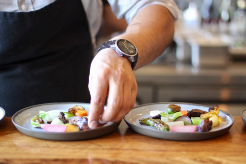 A chef arranges colorful vegetables on two plates in a kitchen setting.