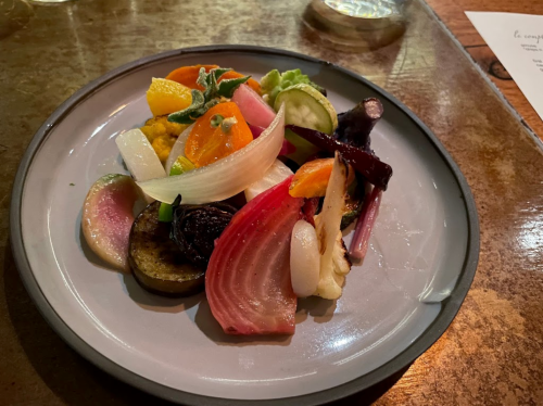 A colorful plate of assorted roasted vegetables, garnished with fresh herbs and citrus slices, on a rustic table.