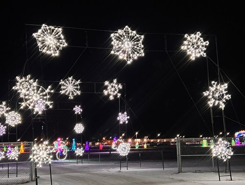 A winter scene featuring illuminated snowflake decorations against a dark night sky, with colorful lights in the background.