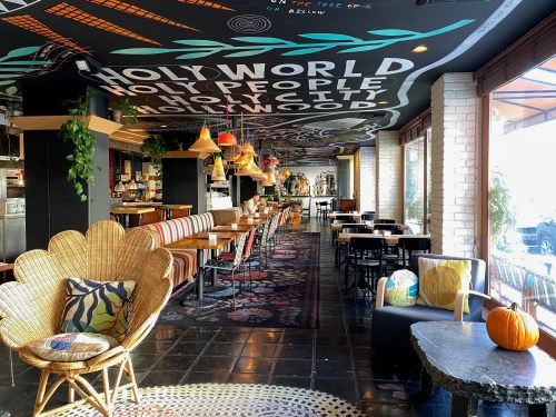 A vibrant restaurant interior featuring colorful decor, unique seating, and a mural on the ceiling.