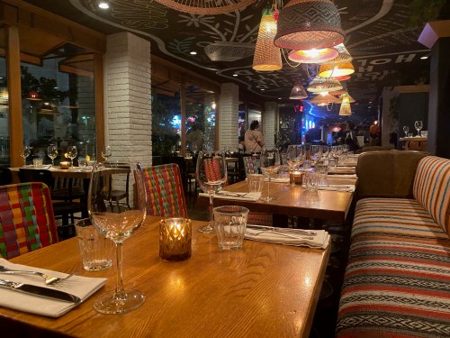 Cozy restaurant interior with colorful seating, tables set with glassware, and warm lighting creating an inviting atmosphere.