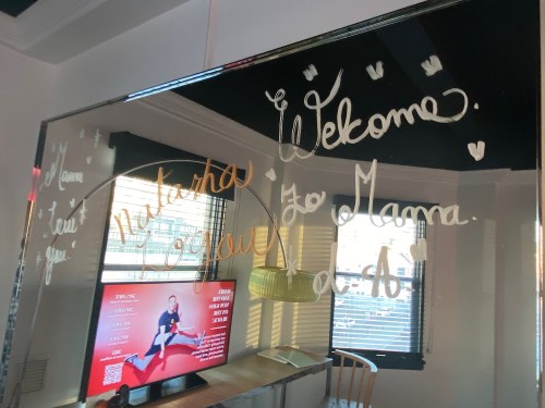 A mirror with handwritten messages saying "Welcome" and "Mama, love you!" alongside a TV displaying a fitness program.