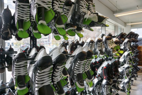 A display of various ice hockey skates in black and green, neatly arranged on shelves.