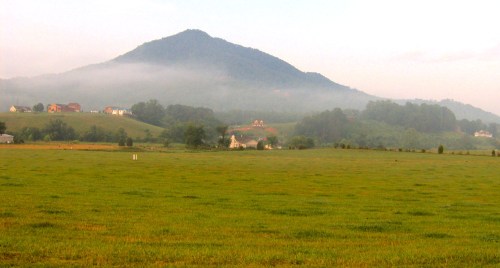 A misty landscape featuring rolling hills, a mountain in the background, and a serene green field in the foreground.