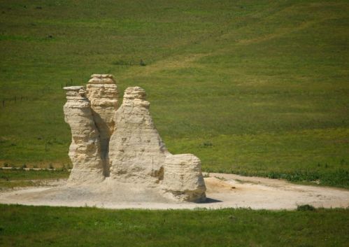 Three tall, white rock formations stand in a green, grassy landscape under a clear blue sky.