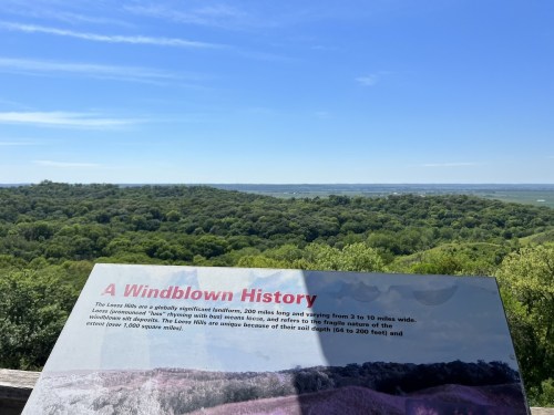 A scenic view of rolling green hills with a sign about the Loess Hills' history and geography in the foreground.