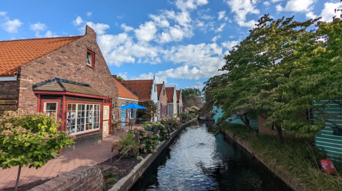 Charming canal lined with quaint houses and greenery under a blue sky with scattered clouds.