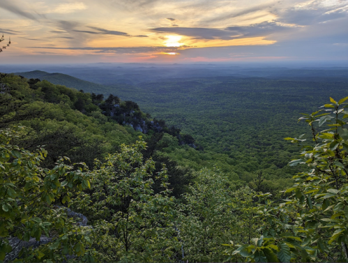 A scenic view of a sunset over lush green mountains, with a colorful sky and distant hills.
