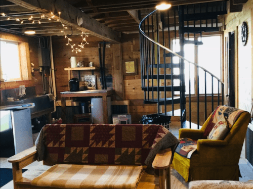 Cozy wooden cabin interior with a spiral staircase, a sofa, and warm lighting.