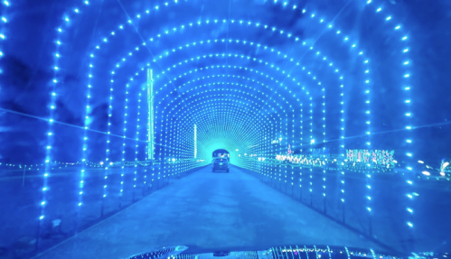 A car drives through a vibrant blue light tunnel, creating a mesmerizing illuminated pathway.