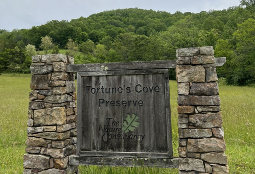 Sign for Fortune's Cove Preserve, featuring stone pillars and surrounded by green hills and trees.