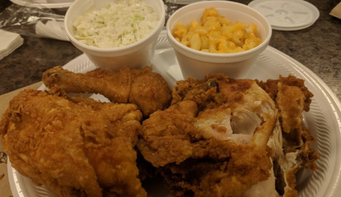 A plate of fried chicken with two sides: coleslaw and macaroni and cheese in white cups.