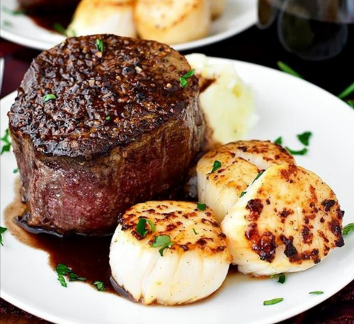A plate featuring a perfectly cooked filet mignon with scallops and mashed potatoes, garnished with herbs.