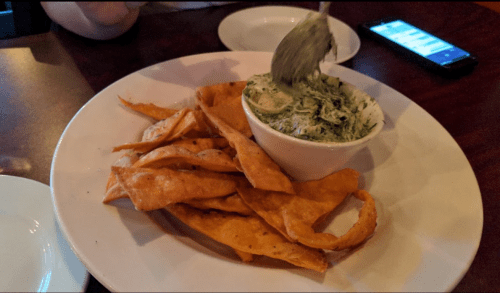 A plate of crispy tortilla chips next to a bowl of creamy spinach dip.