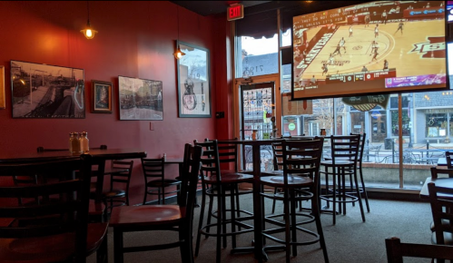 A cozy bar interior with empty chairs, a large screen showing a basketball game, and framed photos on the walls.