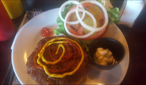 A plate with a burger topped with ketchup and mustard, alongside a fresh salad of lettuce, tomato, and onion.