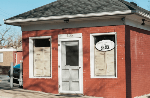 A small red brick building with a sign reading "The Shack" and boarded-up windows.