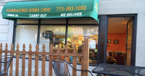 Exterior of Huaraches Doña Chio restaurant with a green awning, wooden fence, and outdoor seating.
