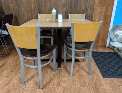 A small wooden table with four chairs in a casual dining setting, featuring condiments on the table.