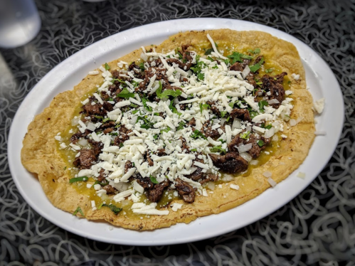 A large plate of tacos topped with seasoned meat, cheese, and fresh herbs on a crispy tortilla.