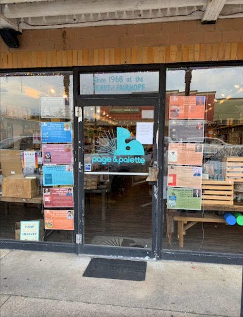 Entrance of Page & Palette bookstore in Fairhope, featuring colorful posters and a welcoming sign.