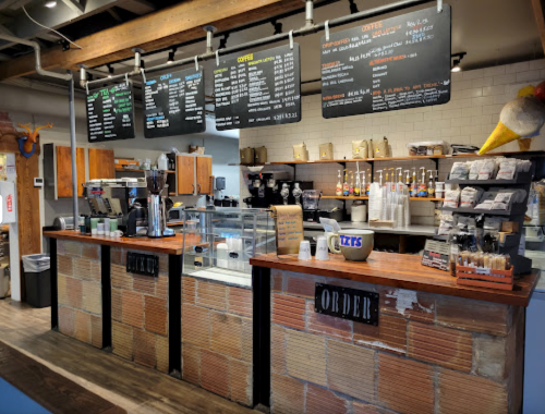 A cozy café counter with menus overhead, coffee equipment, and a display of pastries and drinks.