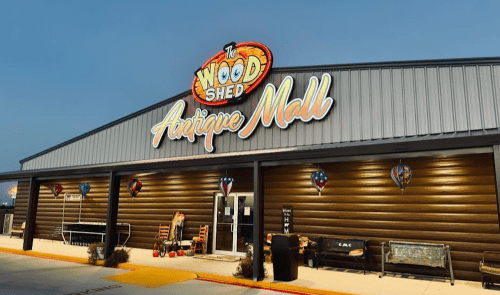 Exterior of "The Wood Shed Antique Mall" with colorful signage and decorative elements, set against a twilight sky.