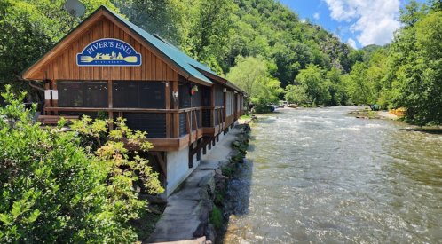 A wooden riverside building labeled "River's End" surrounded by lush greenery and flowing water under a blue sky.