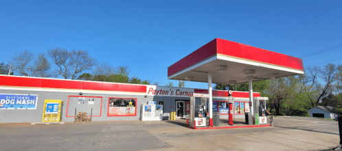 A gas station with a red and white exterior, featuring a convenience store and a self-serve dog wash area.